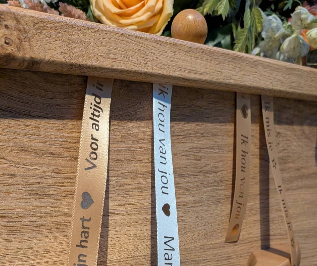 Sfeerbeeld van het lintenritueel waarbij de verbonden linten uit de gesloten uitvaartkist hangen, symbool voor blijvende verbondenheid.